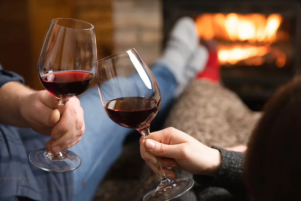 couple sitting by a cozy fire with red wine