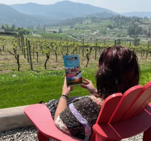 woman on red chair reading a wine guide overlooking a vineyard